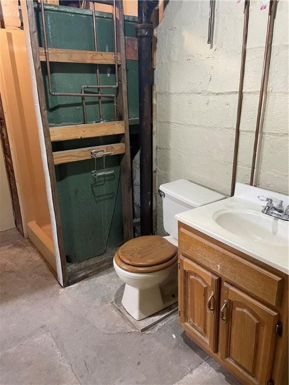 bathroom featuring concrete block wall, unfinished concrete floors, toilet, and vanity