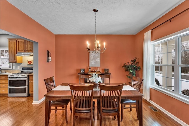 dining area featuring a notable chandelier, light hardwood / wood-style flooring, and a textured ceiling