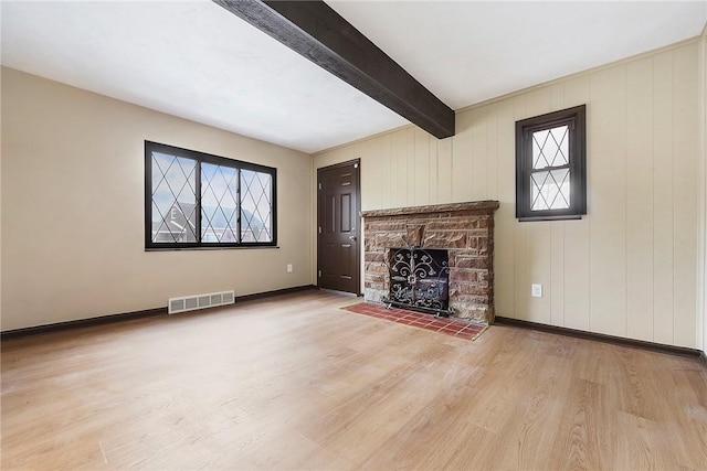 unfurnished living room featuring wood-type flooring, a stone fireplace, and beam ceiling