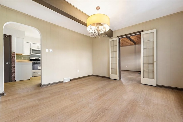 empty room with french doors, a chandelier, and light hardwood / wood-style flooring