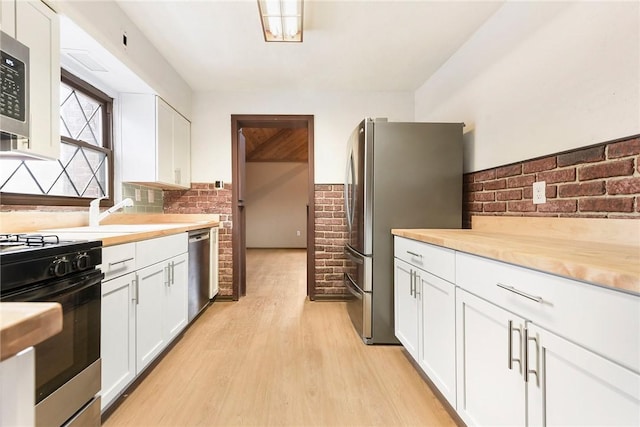 kitchen with stainless steel appliances, brick wall, white cabinets, and light hardwood / wood-style flooring