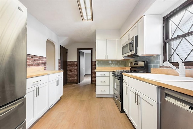 kitchen featuring appliances with stainless steel finishes, butcher block countertops, sink, white cabinets, and light hardwood / wood-style floors