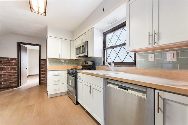 kitchen with sink, white cabinets, decorative backsplash, stainless steel appliances, and light wood-type flooring