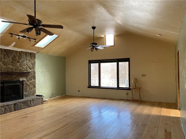 unfurnished living room featuring a fireplace, lofted ceiling with skylight, ceiling fan, and light wood-type flooring