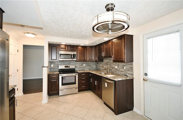 kitchen featuring sink, hanging light fixtures, stainless steel appliances, light stone countertops, and dark brown cabinets