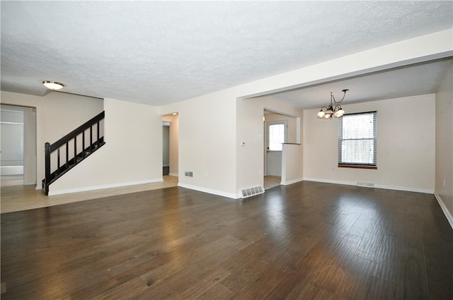 unfurnished living room featuring an inviting chandelier, dark hardwood / wood-style flooring, and a textured ceiling