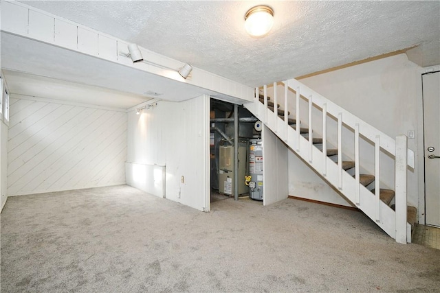 basement with water heater, carpet flooring, a textured ceiling, and wood walls