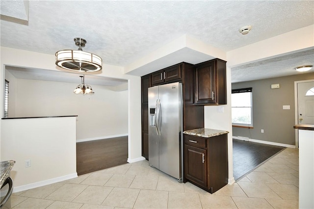 kitchen featuring pendant lighting, stainless steel fridge, light tile patterned flooring, and dark brown cabinets