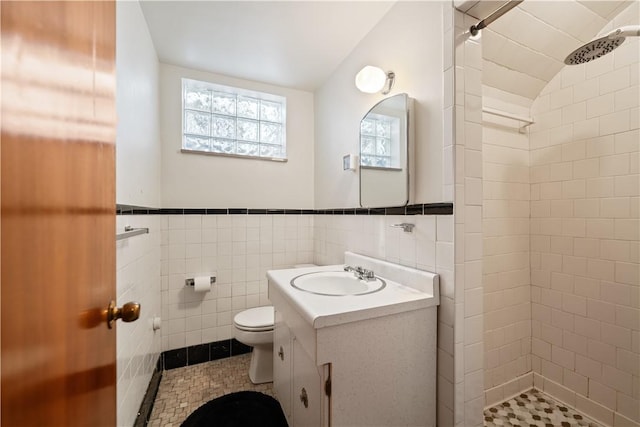 bathroom with tile walls, vanity, a tile shower, tile patterned floors, and toilet