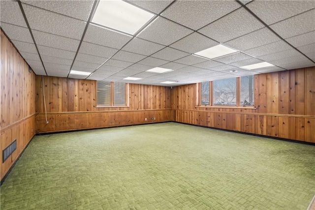 basement with a drop ceiling and wooden walls