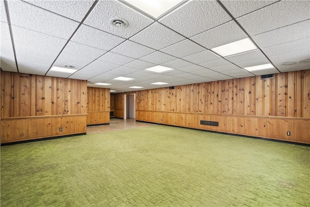 basement with a drop ceiling and wood walls