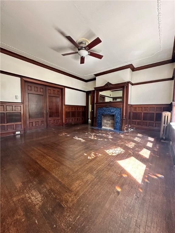 unfurnished living room featuring a tile fireplace, crown molding, dark hardwood / wood-style floors, and ceiling fan