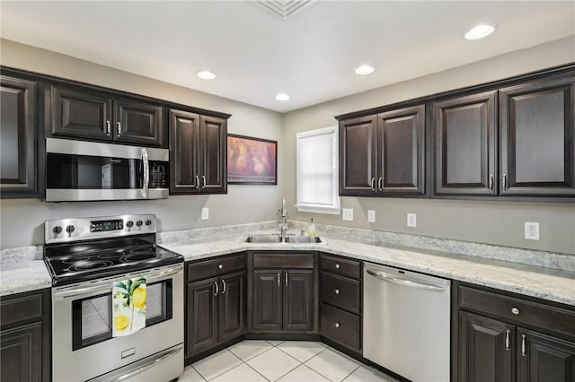 kitchen featuring appliances with stainless steel finishes, sink, light tile patterned floors, light stone counters, and dark brown cabinets