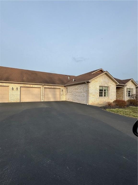 exterior space with aphalt driveway, an attached garage, and brick siding