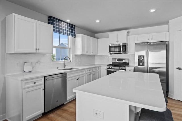 kitchen with sink, appliances with stainless steel finishes, white cabinetry, a kitchen island, and dark hardwood / wood-style flooring