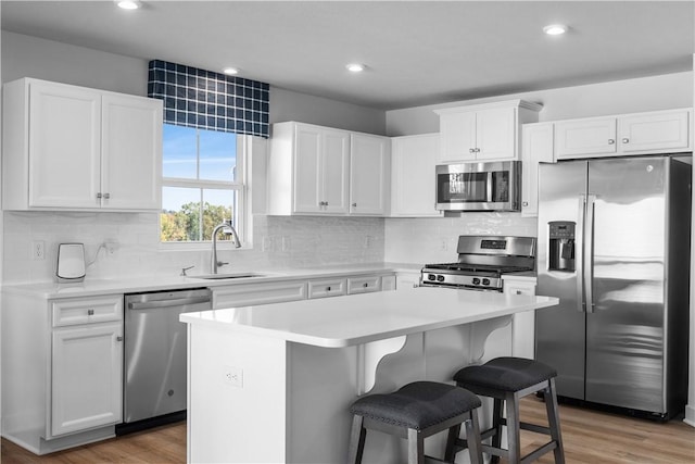 kitchen featuring sink, stainless steel appliances, wood-type flooring, white cabinets, and a kitchen island