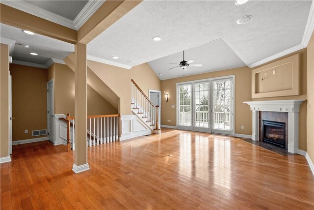 unfurnished living room with hardwood / wood-style floors, lofted ceiling, a tiled fireplace, ceiling fan, and crown molding