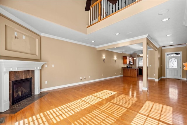 unfurnished living room featuring a tiled fireplace, hardwood / wood-style floors, and ornamental molding