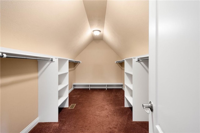 walk in closet with dark carpet and vaulted ceiling