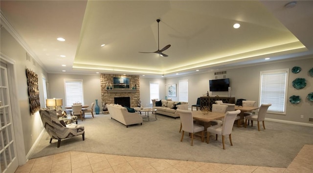 interior space with a stone fireplace, ornamental molding, a raised ceiling, and ceiling fan