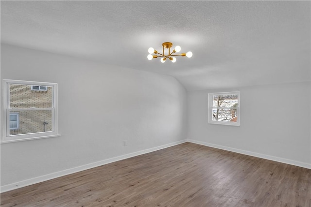 unfurnished room with hardwood / wood-style flooring, lofted ceiling, a notable chandelier, and a textured ceiling