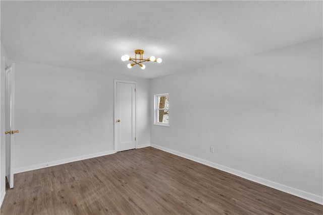 empty room featuring dark wood-type flooring, a textured ceiling, and a notable chandelier