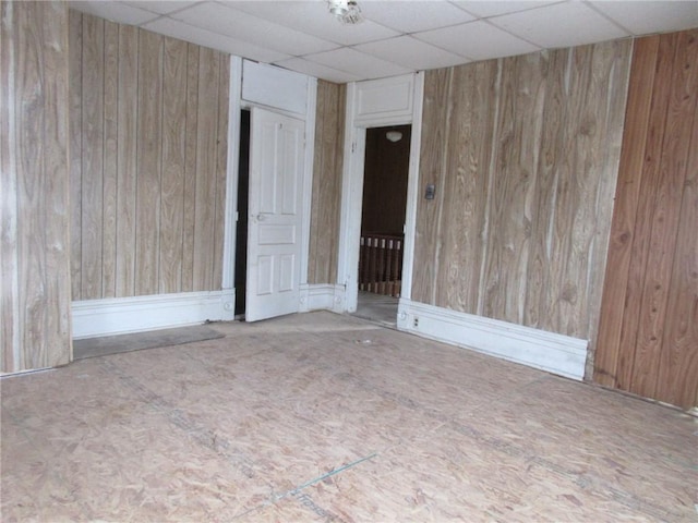 spare room with a paneled ceiling and wooden walls