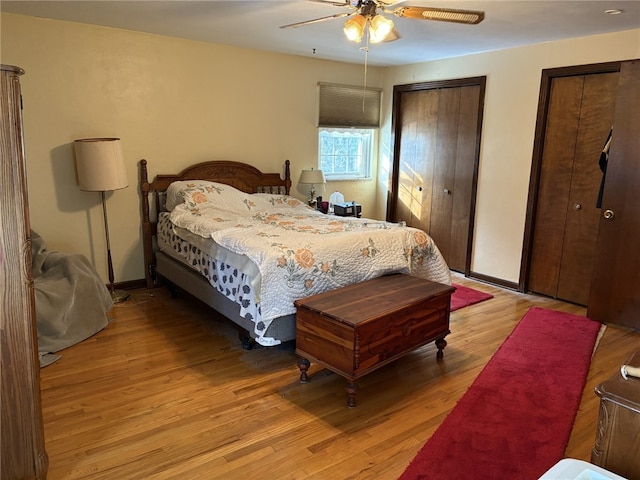 bedroom with ceiling fan, light hardwood / wood-style floors, and two closets