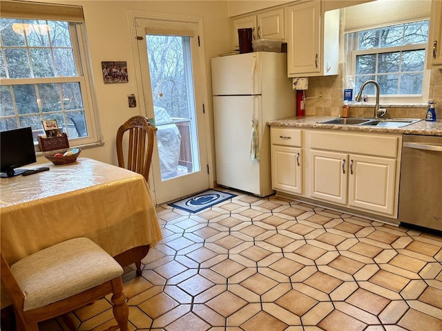 kitchen featuring sink, backsplash, white fridge, stainless steel dishwasher, and a healthy amount of sunlight