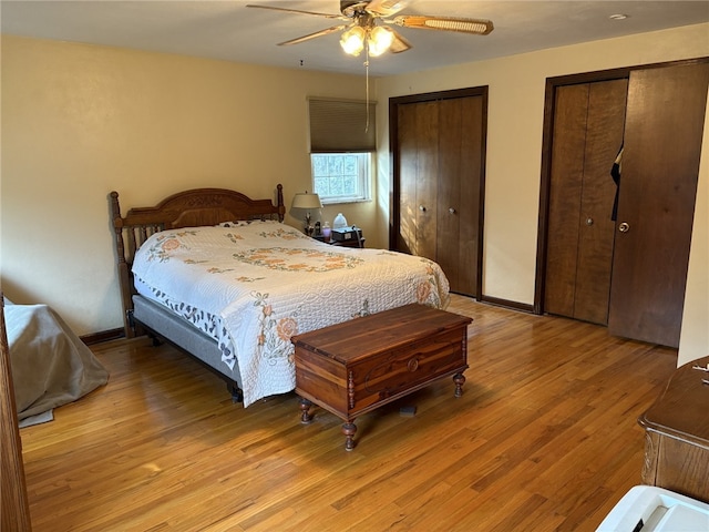 bedroom with light wood-type flooring, two closets, a ceiling fan, and baseboards