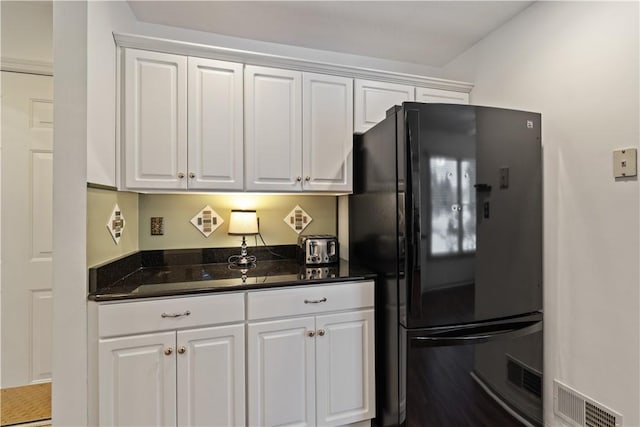 kitchen featuring black refrigerator, white cabinetry, and dark stone countertops