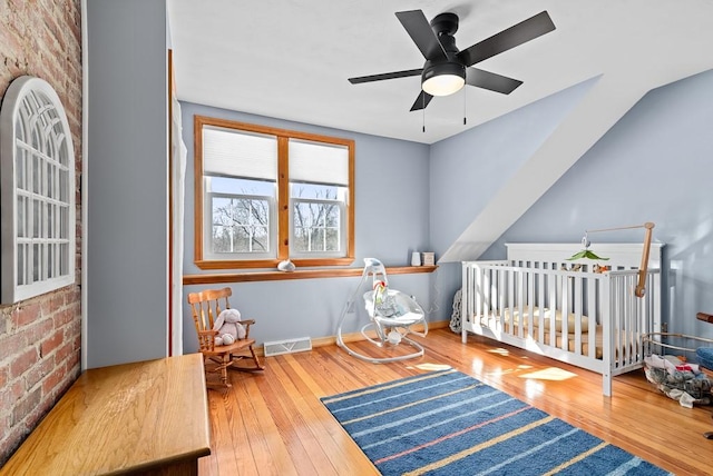 bedroom with brick wall, a nursery area, hardwood / wood-style floors, and ceiling fan