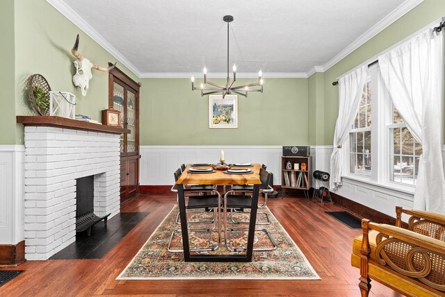 dining area featuring an inviting chandelier, a brick fireplace, crown molding, and dark hardwood / wood-style floors