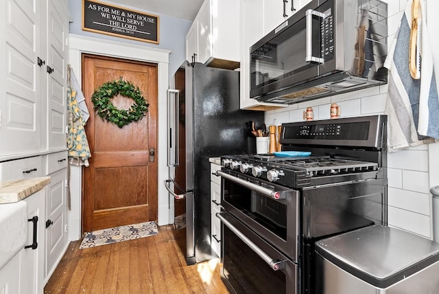 kitchen with white cabinetry, hardwood / wood-style floors, tasteful backsplash, and range with two ovens