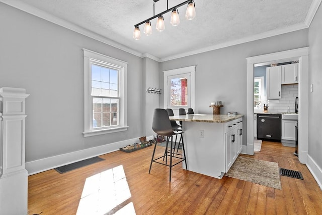 kitchen featuring dishwasher, a breakfast bar area, white cabinets, hanging light fixtures, and light hardwood / wood-style floors