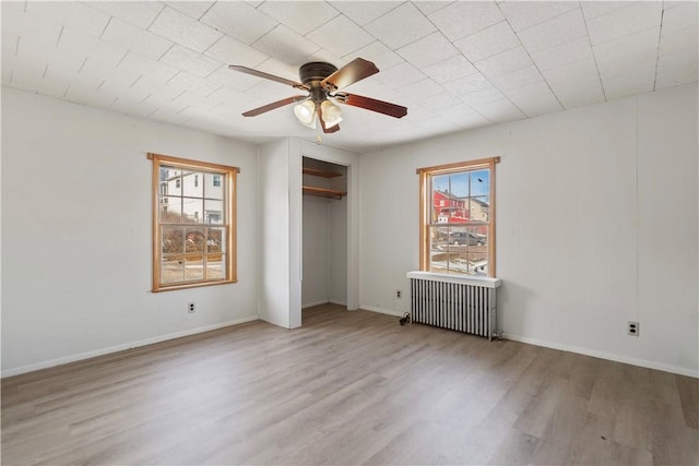 unfurnished bedroom with ceiling fan, radiator, light hardwood / wood-style floors, and a closet