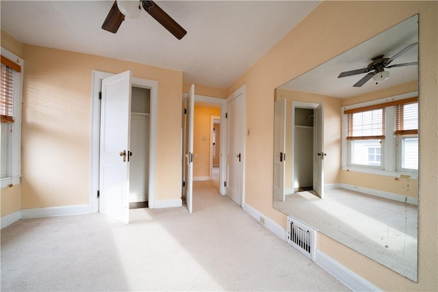 unfurnished bedroom with ceiling fan, light colored carpet, and multiple closets