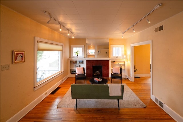 living room with rail lighting, a brick fireplace, and light wood-type flooring