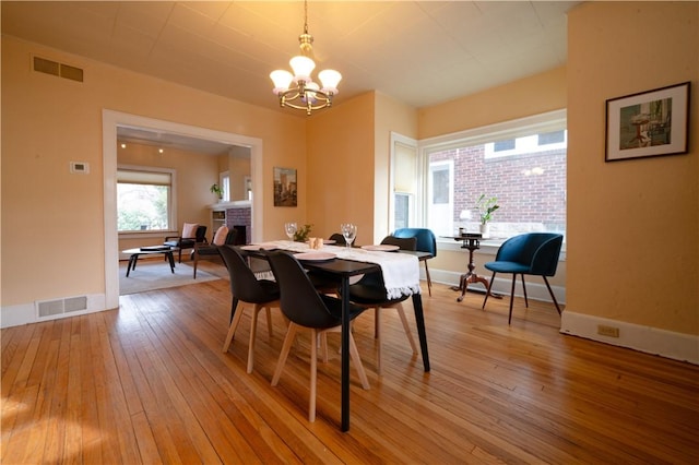 dining space with wood-type flooring, a fireplace, and a notable chandelier