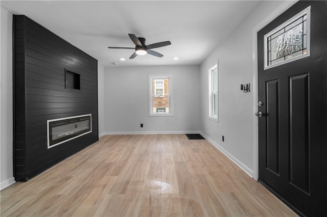 unfurnished living room with ceiling fan, a large fireplace, and light hardwood / wood-style flooring