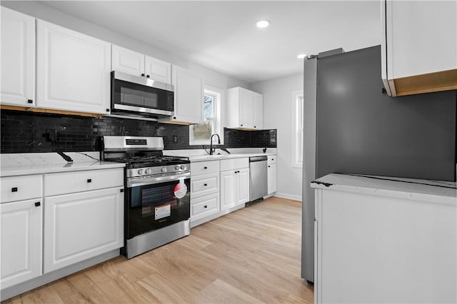 kitchen with light stone counters, stainless steel appliances, white cabinets, and light wood-type flooring