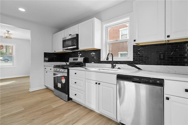 kitchen featuring appliances with stainless steel finishes, sink, white cabinets, light stone counters, and light hardwood / wood-style flooring