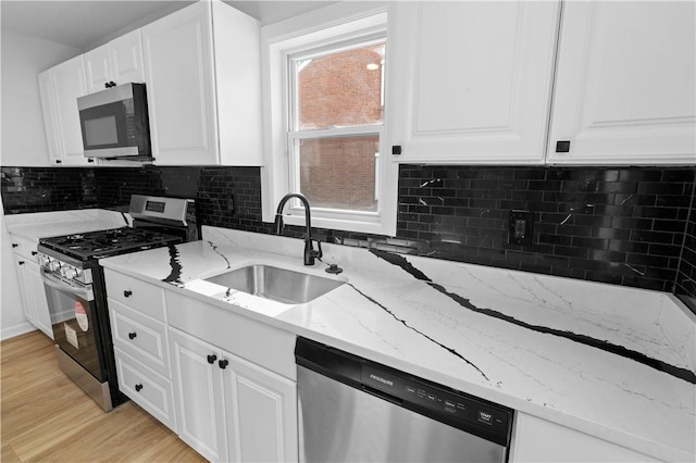 kitchen with white cabinetry, appliances with stainless steel finishes, sink, and light stone counters