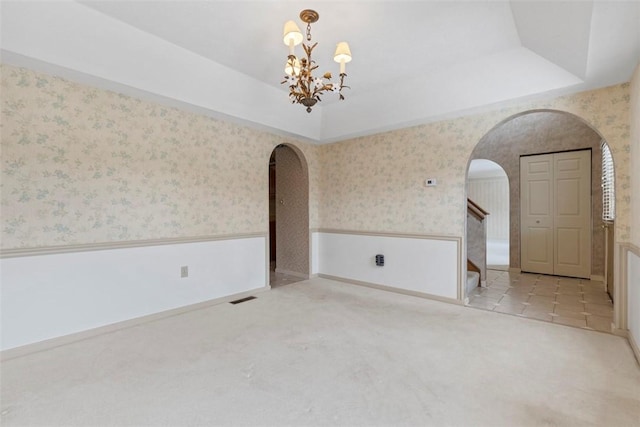 unfurnished room featuring a raised ceiling and an inviting chandelier