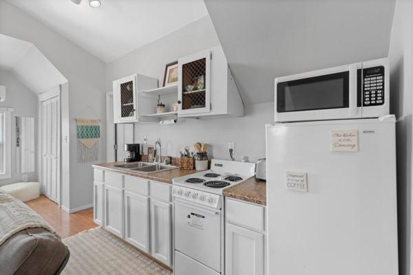 kitchen with lofted ceiling, sink, light hardwood / wood-style flooring, white appliances, and white cabinets