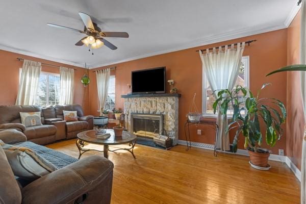 living room with crown molding, ceiling fan, wood-type flooring, and a fireplace