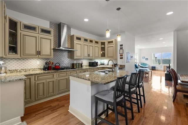 kitchen featuring a kitchen bar, sink, decorative light fixtures, a kitchen island with sink, and wall chimney range hood