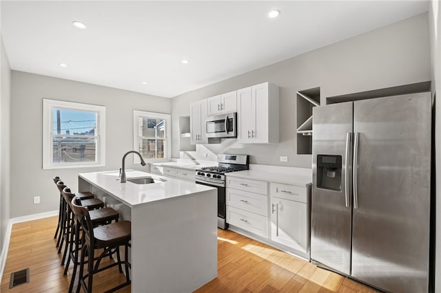 kitchen featuring appliances with stainless steel finishes, white cabinetry, sink, a kitchen breakfast bar, and a center island with sink