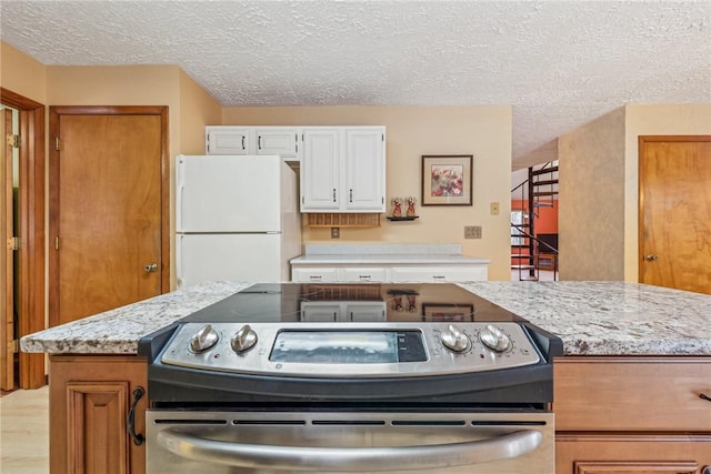 kitchen featuring white cabinetry, stainless steel range with electric stovetop, light stone countertops, a textured ceiling, and white fridge