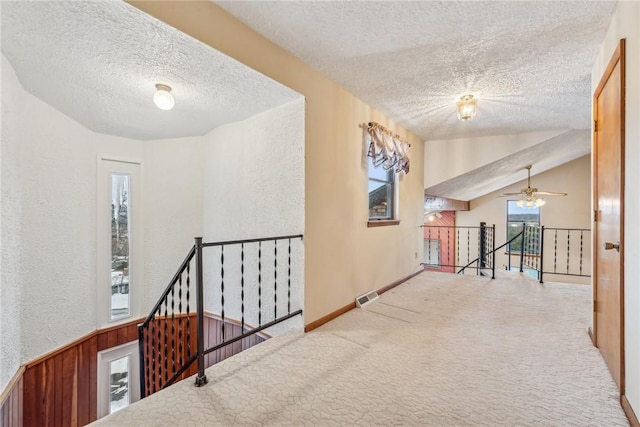 corridor featuring vaulted ceiling, light colored carpet, and a textured ceiling